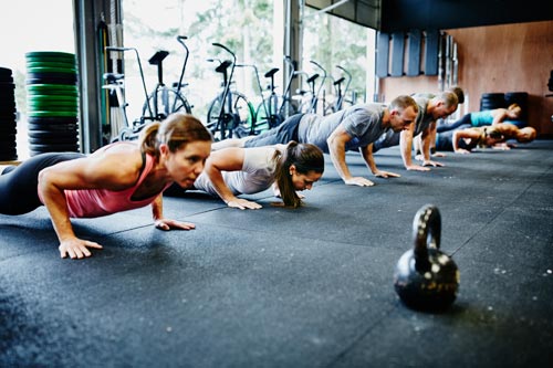 Grupp av unga vuxna tränar tillsammans på ett modernt gym genom att utföra armhävningar i perfekt rad